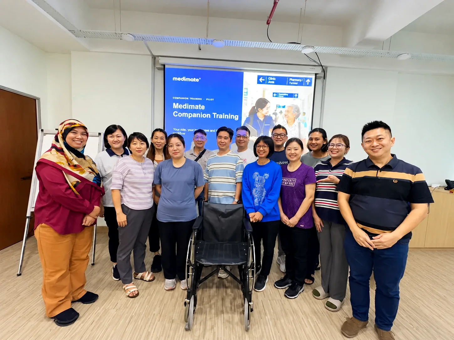 Participants and trainers from Medimate's first Companion training programme standing together in a training room, with a wheelchair at the front and a Medimate Companion Training presentation slide behind them